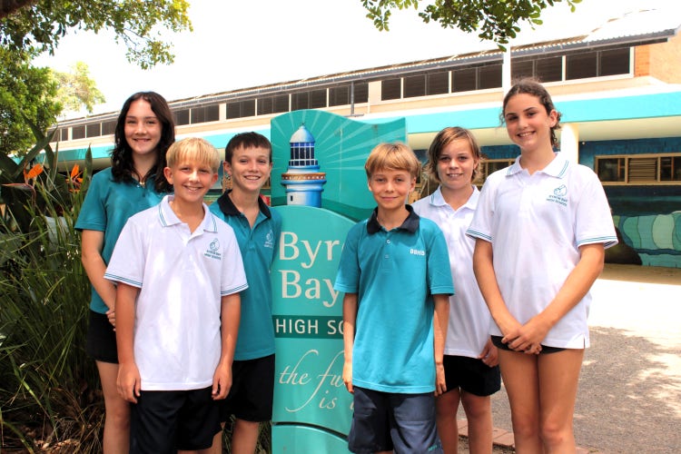 Six students surrounding the teal blue lighthouse sign at the entry to Byron Bay High School
