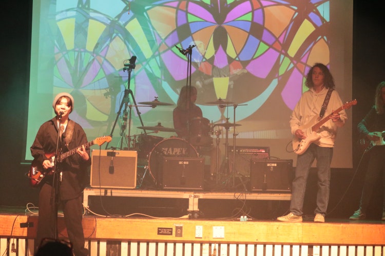 Three students in a band performing on stage in the school hall