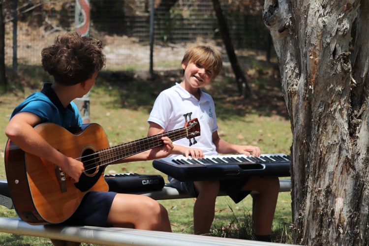 One student playing the guitar, and another on the keyboard practicing music outside in the playground