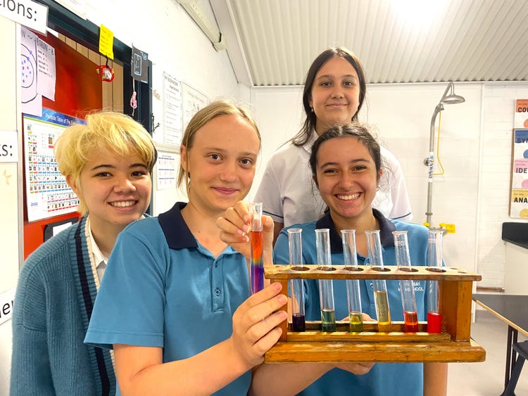 Four students participating in a science experiment and holing test tubes with various coloured liquid