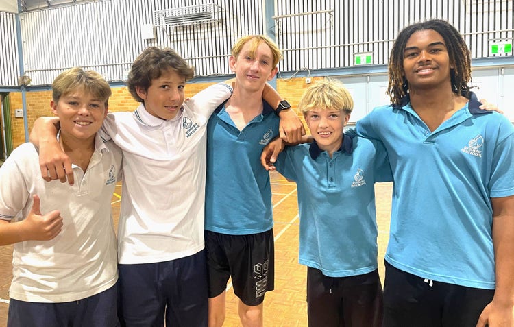 Four boys in the school hall smiling with arms around each other's shoulders after a game of Futsal