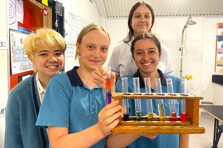 Four students participating in a science experiment and holing test tubes with various coloured liquid